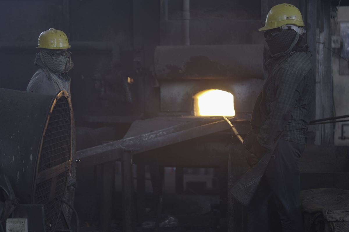 Two forging shop workers in hard hats beside a glowing furnace at the RIC works